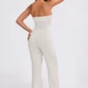 Jumpsuit i grovstickat tyg med bandeau-halsringning och utsvängda byxben i krämfärg Jumpsuit i grovstickat tyg med bandeau-halsringning och utsvängda byxben i krämfärg