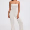 Jumpsuit i grovstickat tyg med bandeau-halsringning och utsvängda byxben i krämfärg Jumpsuit i grovstickat tyg med bandeau-halsringning och utsvängda byxben i krämfärg
